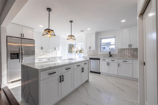 kitchen with a sink, tasteful backsplash, appliances with stainless steel finishes, marble finish floor, and white cabinets