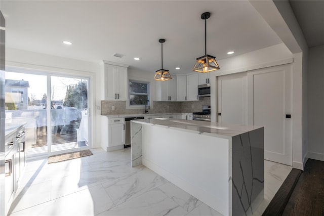 kitchen with recessed lighting, backsplash, marble finish floor, a kitchen island, and appliances with stainless steel finishes