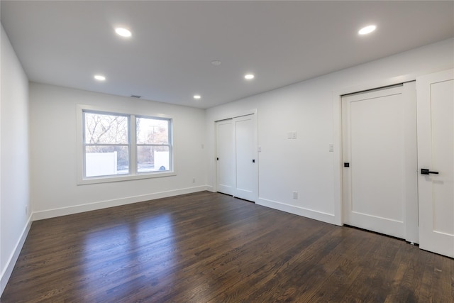 unfurnished bedroom with two closets, recessed lighting, baseboards, and dark wood finished floors