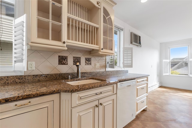 kitchen featuring dishwasher, dark stone counters, cream cabinetry, a sink, and backsplash