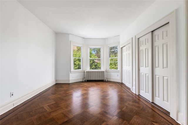 unfurnished bedroom featuring radiator, baseboards, and multiple closets