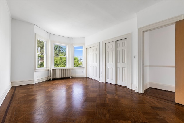 unfurnished bedroom featuring baseboards, radiator, and multiple closets