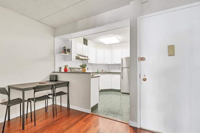 kitchen with open shelves, under cabinet range hood, freestanding refrigerator, white cabinets, and a peninsula