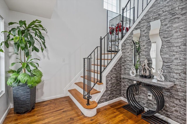 stairway featuring a high ceiling, baseboards, and wood finished floors