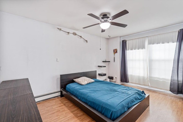 bedroom featuring ceiling fan, a baseboard heating unit, and wood finished floors