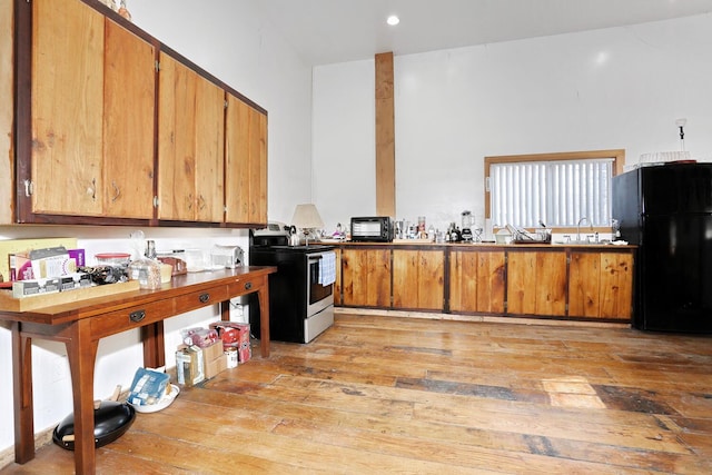 kitchen with electric stove, a sink, light wood-style floors, freestanding refrigerator, and brown cabinets
