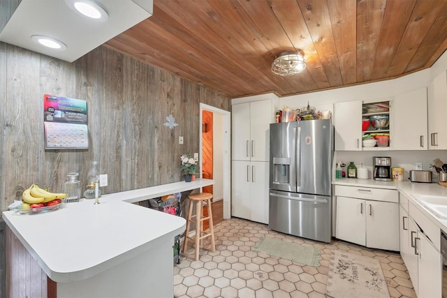 kitchen with wood walls, light countertops, open shelves, wooden ceiling, and stainless steel fridge