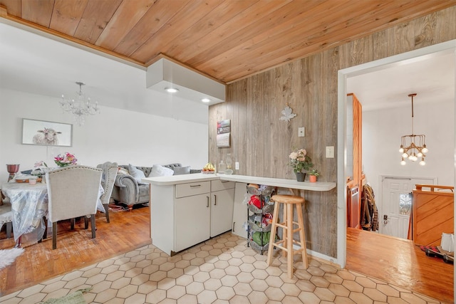 kitchen featuring wood walls, light tile patterned floors, wood ceiling, an inviting chandelier, and a peninsula