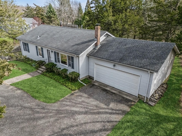 ranch-style home featuring aphalt driveway, a chimney, a shingled roof, and a front lawn