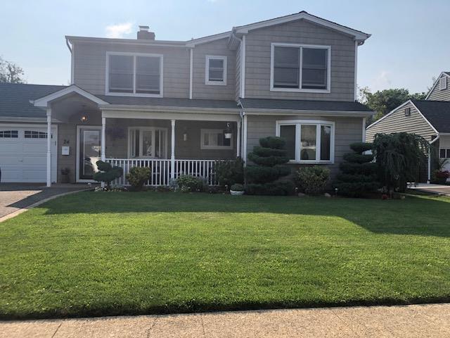 view of front of home with a chimney, covered porch, a front yard, and a garage