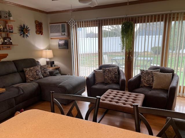 living room with a wall unit AC, ceiling fan, crown molding, and wood finished floors