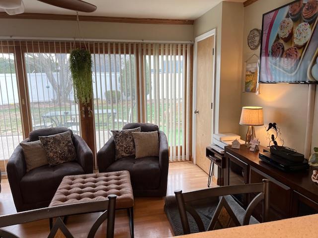 living area with light wood finished floors, ornamental molding, and ceiling fan