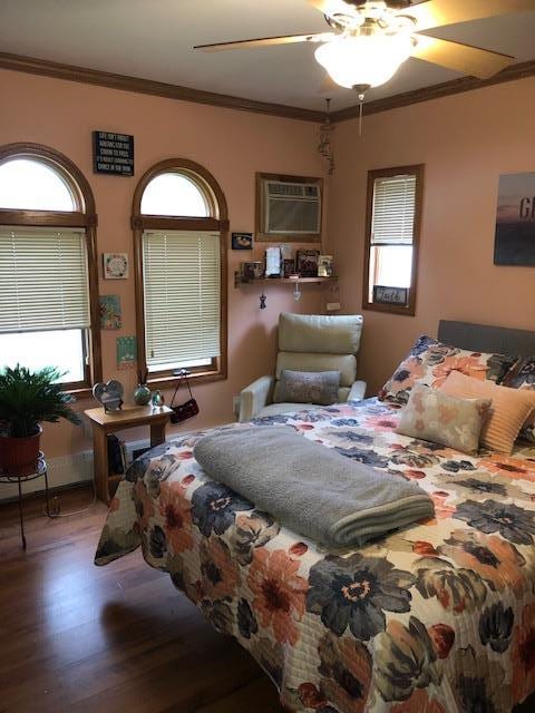 bedroom featuring a ceiling fan, a wall unit AC, wood finished floors, and ornamental molding