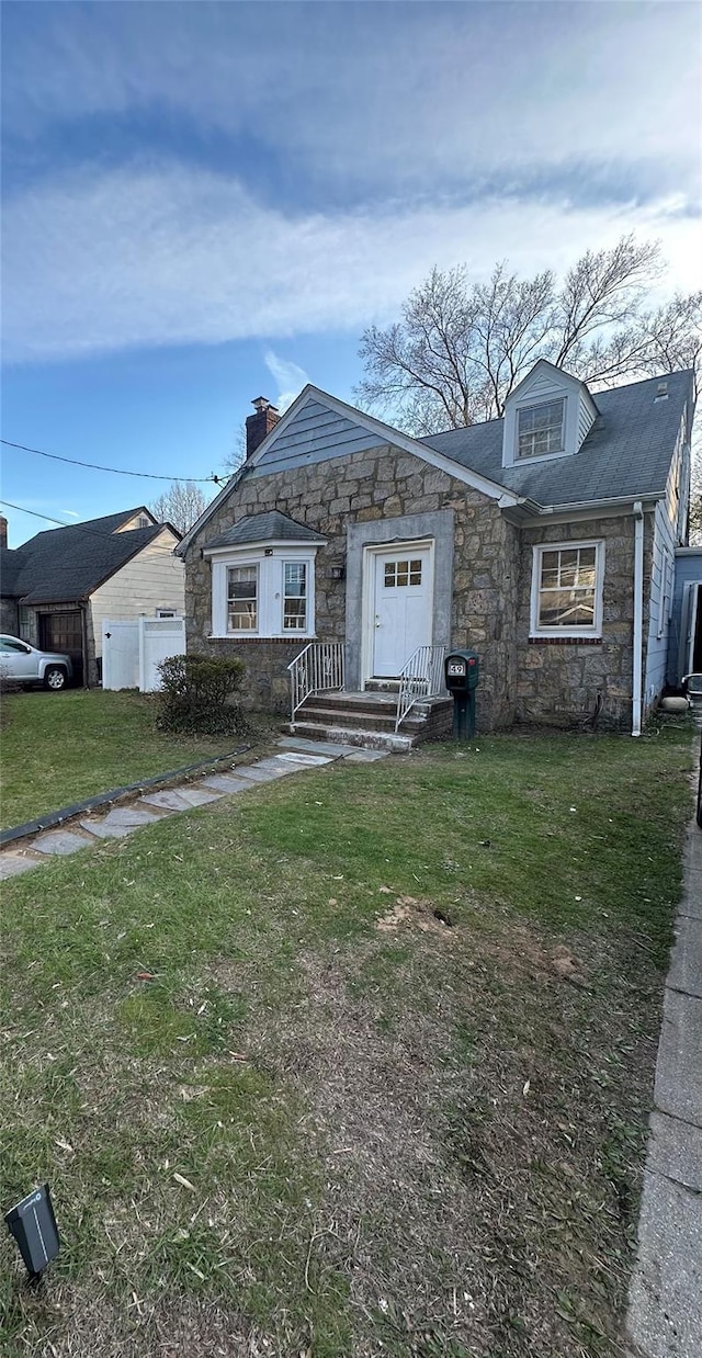 view of front of home with stone siding, a front yard, fence, and a chimney