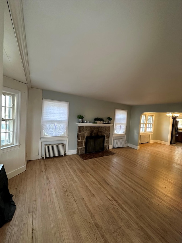 unfurnished living room featuring radiator, light wood-style floors, a fireplace, and baseboards