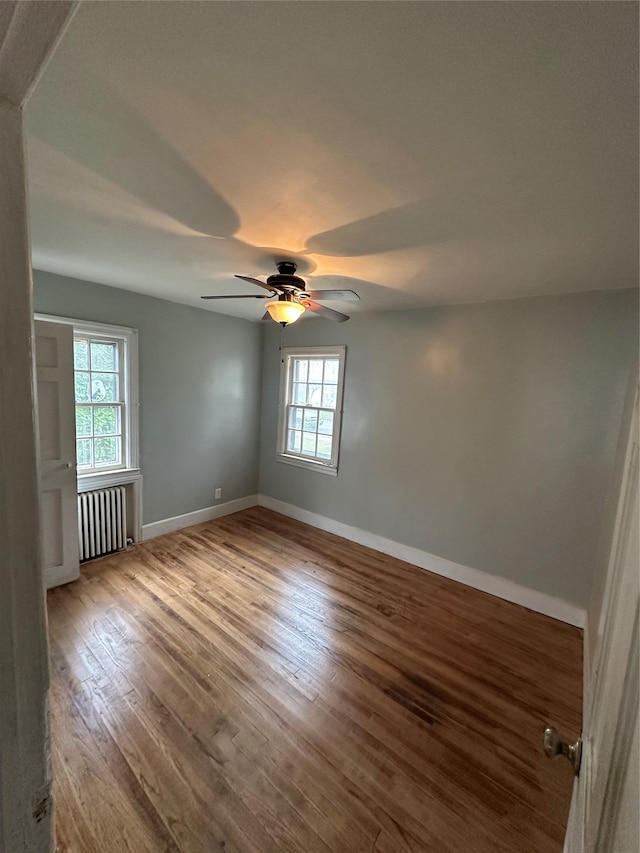 unfurnished room featuring radiator, wood finished floors, a wealth of natural light, and baseboards
