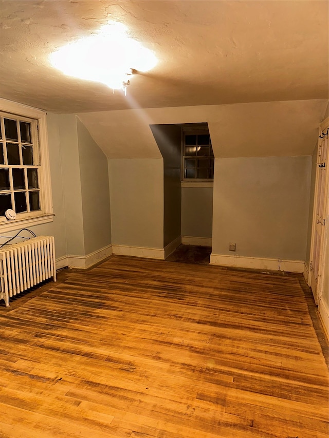 additional living space with radiator, lofted ceiling, wood finished floors, and baseboards