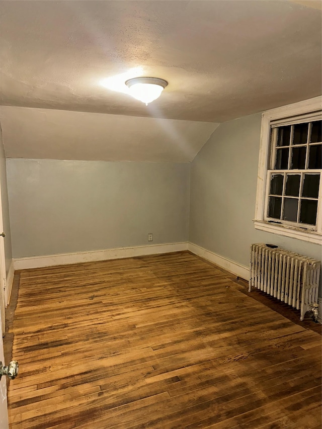 bonus room featuring a textured ceiling, baseboards, radiator, vaulted ceiling, and wood finished floors