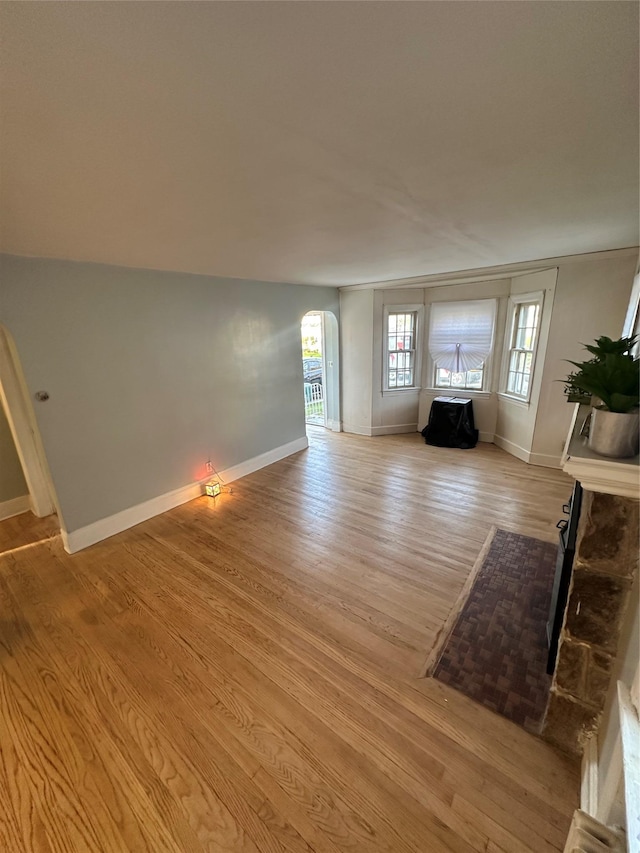 unfurnished living room featuring light wood finished floors, arched walkways, and baseboards