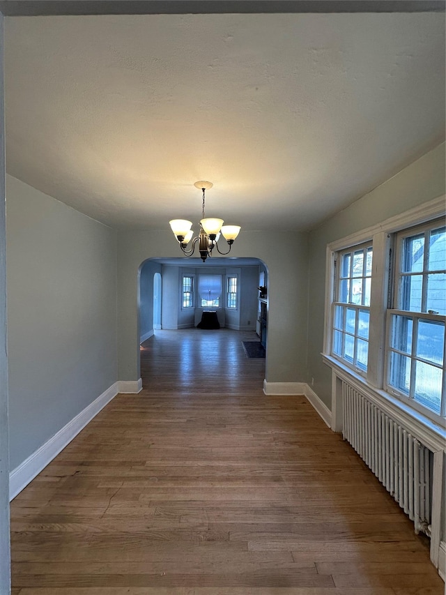 unfurnished dining area featuring wood finished floors, a chandelier, and arched walkways