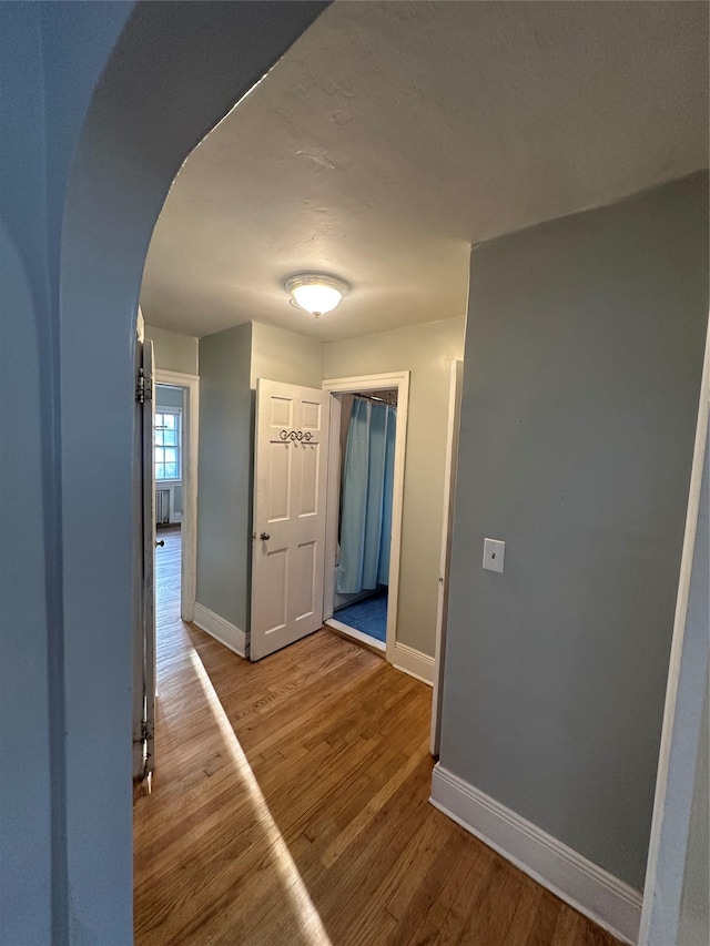 hallway with arched walkways, wood finished floors, and baseboards