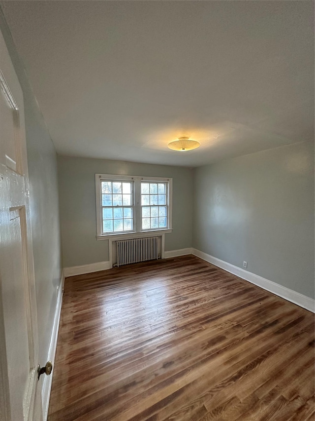 empty room featuring radiator, wood finished floors, and baseboards
