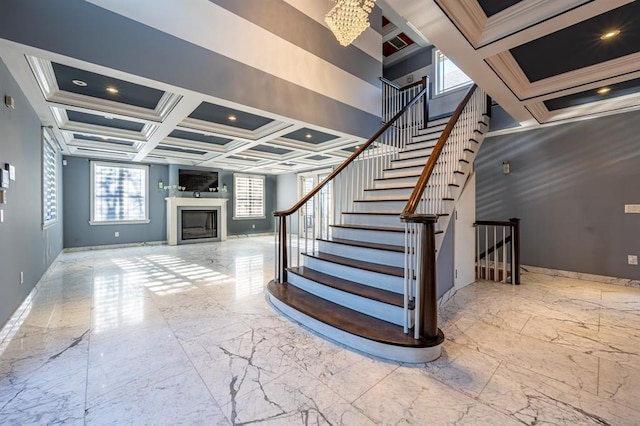 stairway featuring baseboards, marble finish floor, a glass covered fireplace, an inviting chandelier, and coffered ceiling