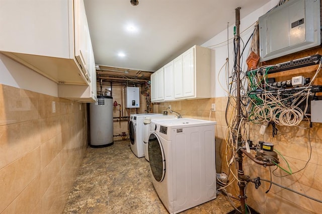 washroom featuring electric panel, gas water heater, water heater, washing machine and dryer, and cabinet space