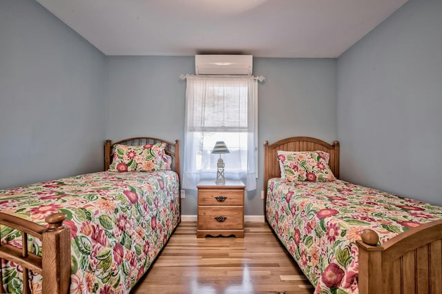bedroom featuring light wood-style floors, a wall mounted AC, and baseboards