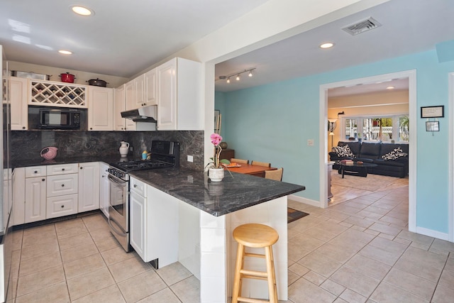kitchen with visible vents, black microwave, stainless steel gas range, a peninsula, and under cabinet range hood