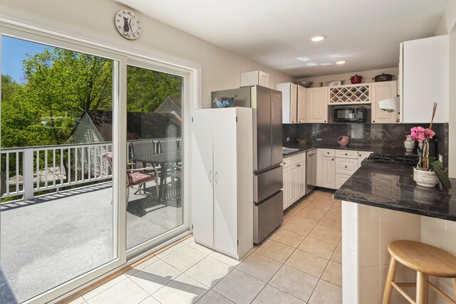 kitchen with light tile patterned flooring, dark stone counters, under cabinet range hood, tasteful backsplash, and appliances with stainless steel finishes