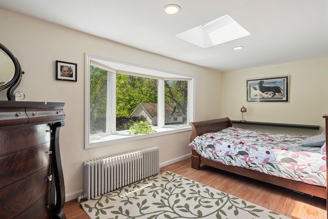 bedroom with radiator heating unit, baseboards, a skylight, and wood finished floors
