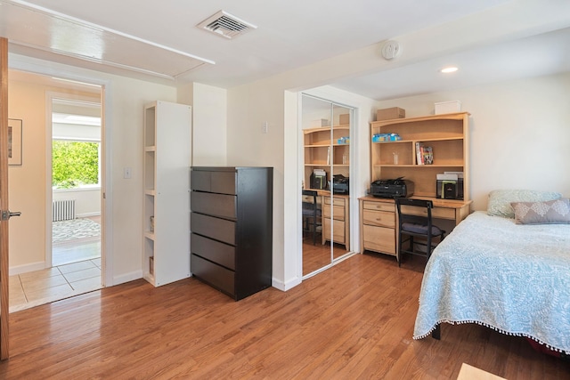 bedroom featuring radiator, attic access, light wood-style flooring, and visible vents