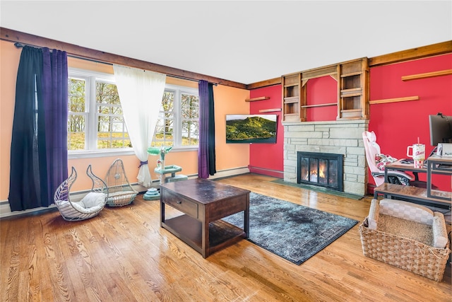 living room featuring baseboards, wood finished floors, and a stone fireplace