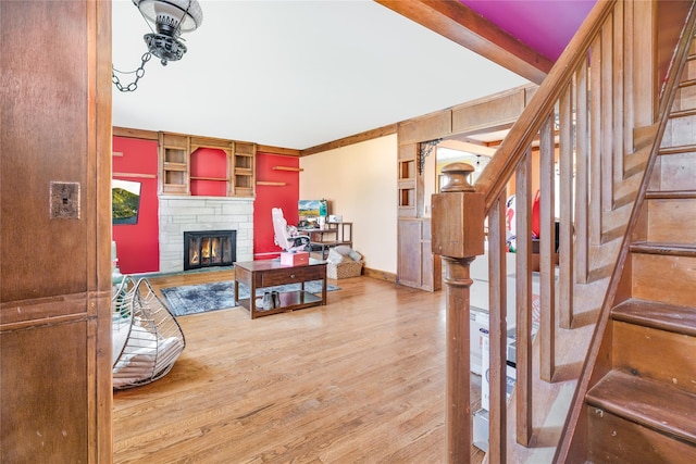 living room with wood finished floors, beamed ceiling, a stone fireplace, baseboards, and stairway