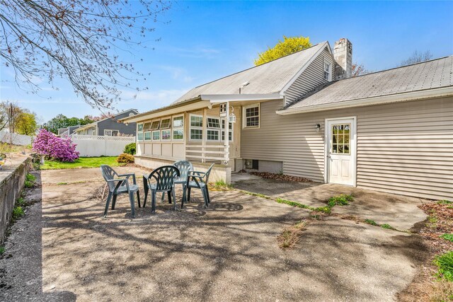 back of property featuring fence, a chimney, metal roof, and a patio