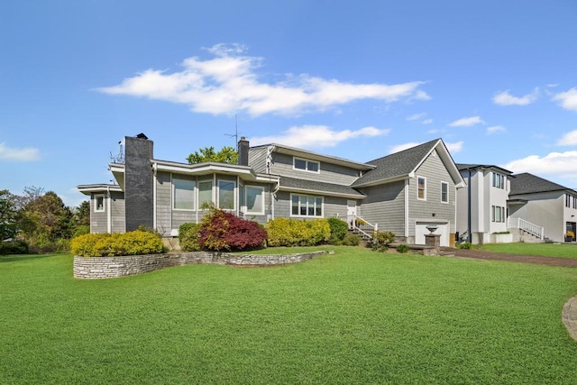 rear view of property with a lawn, a chimney, an attached garage, stairway, and aphalt driveway