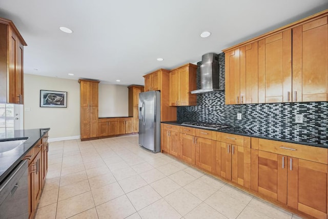 kitchen with brown cabinets, dark stone counters, stainless steel appliances, backsplash, and wall chimney range hood