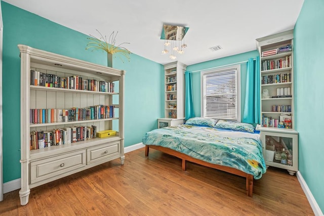 bedroom featuring a notable chandelier, baseboards, visible vents, and wood finished floors