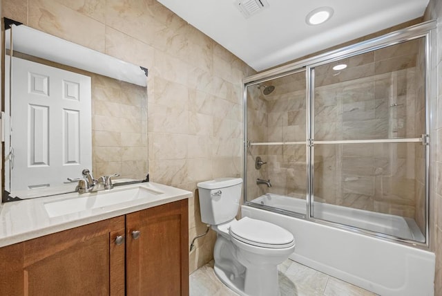 full bathroom with tile walls, bath / shower combo with glass door, toilet, visible vents, and vanity