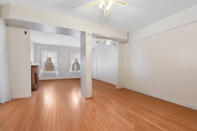 unfurnished living room with a fireplace, light wood-style flooring, baseboards, and a ceiling fan