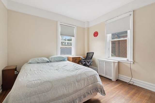 bedroom with radiator heating unit, hardwood / wood-style flooring, and baseboards