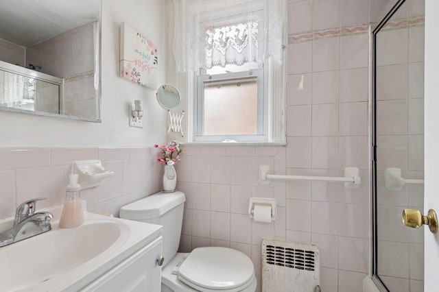 bathroom featuring a shower with door, vanity, toilet, radiator heating unit, and tile walls