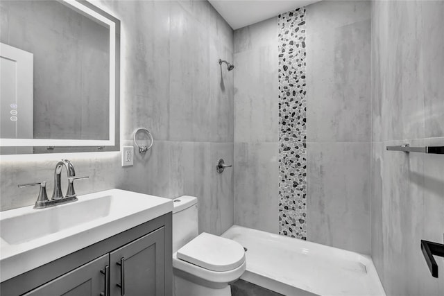 bathroom with tile walls, toilet, tiled shower, and vanity