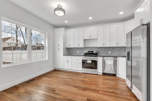 kitchen with tasteful backsplash, appliances with stainless steel finishes, visible vents, dark countertops, and light wood-style floors