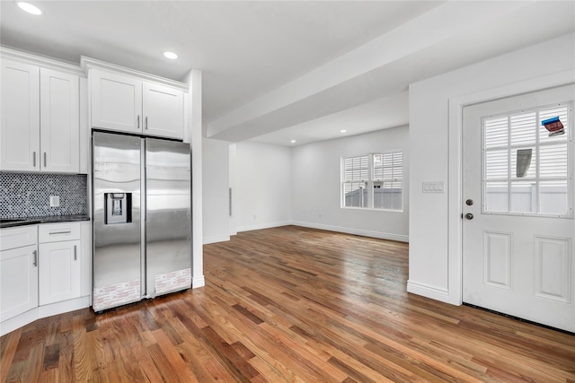 kitchen featuring white cabinetry, tasteful backsplash, stainless steel refrigerator with ice dispenser, dark countertops, and wood finished floors