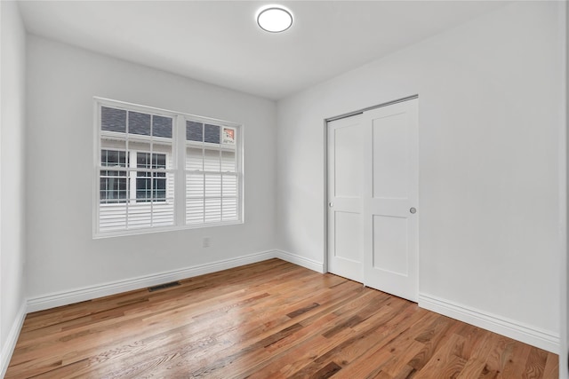 unfurnished bedroom with baseboards, a closet, light wood finished floors, and visible vents