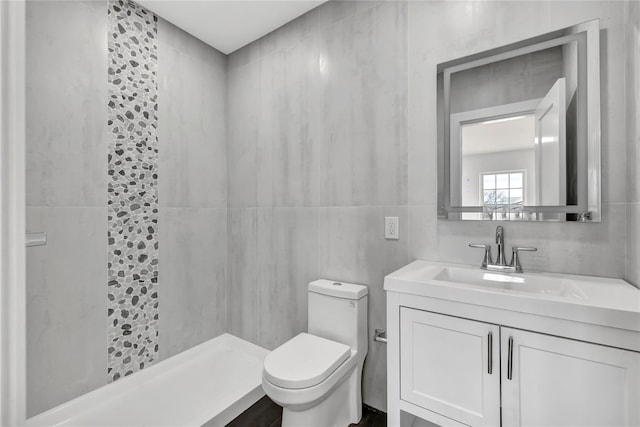 bathroom with tile walls, toilet, tiled shower, and vanity