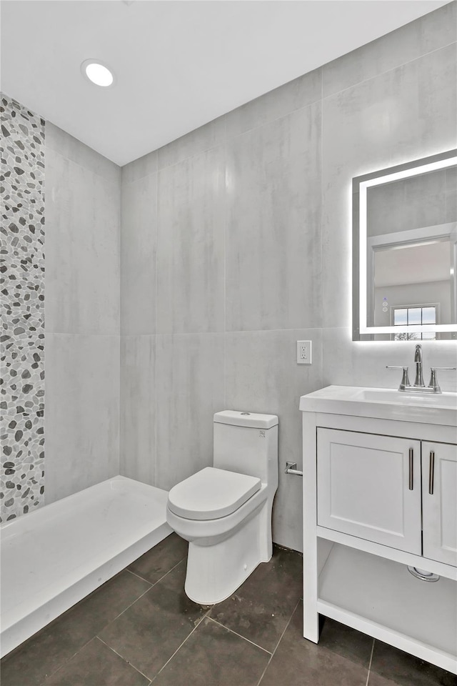 bathroom with tile walls, toilet, vanity, tiled shower, and tile patterned flooring