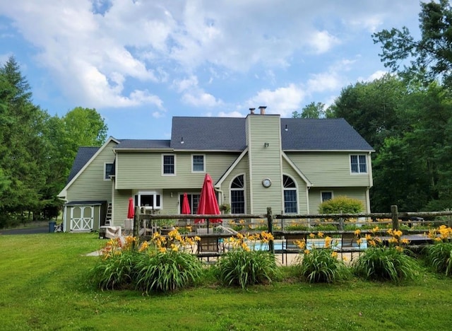rear view of property featuring fence, a garage, a deck, a chimney, and a yard